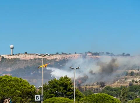Yellow fire-fighting plane is throwing water on fire Stock Photos