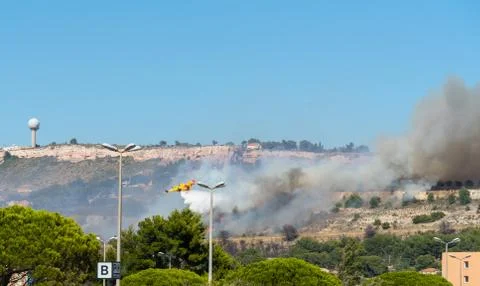 Yellow fire-fighting plane is throwing water on fire Stock Photos