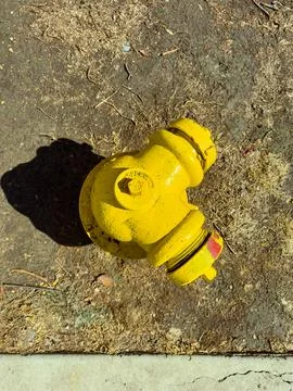 Yellow fire hydrant sits on dry ground near sidewalk with shadow reaching o.. Foto stock