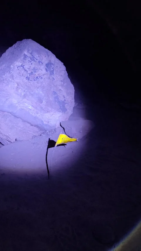 Yellow flag marks research site in dark cave, lit by flashlight during explore Stock Footage 310142918
