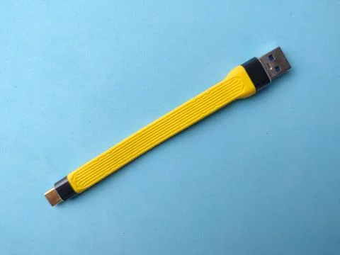 A yellow flat USB charging and data cable is laid diagonally against a smoo.. Fotos Stock