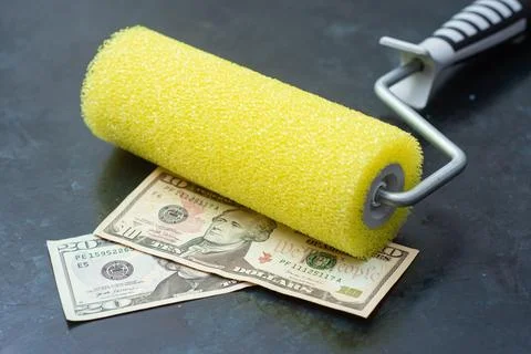 Yellow foam paint roller placed on ten and twenty dollar bills on dark back.. Stock Photos