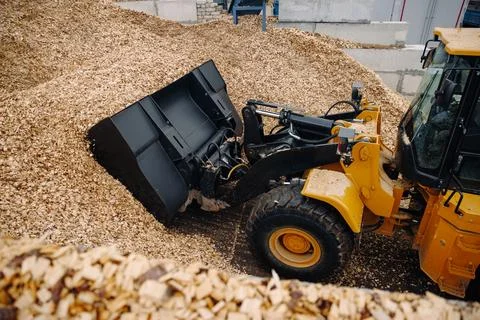 Yellow front-end loader machinery scooping wood chips in a construction site Stock Photos