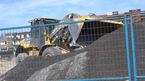 Yellow front end loader moving a pile of crushed gravel behind a blue metal Stock Footage 334673023