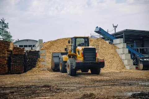 Yellow front-end loader positioned in a lumber yard, moving wood chips near a Stock Photos