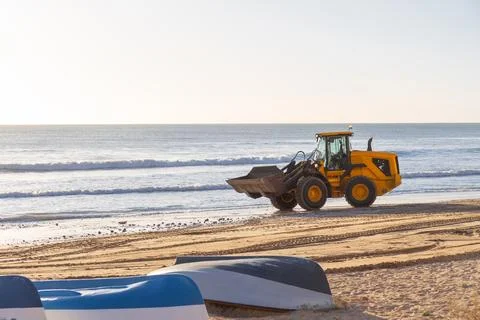 A yellow front-end loader works on the sandy shore of the Mediterranean sea.. Stock Photos