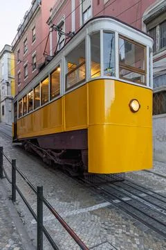 A yellow funicular tram, the Elevador da Gloria, ascends a steep, cobbled str Stock Photos