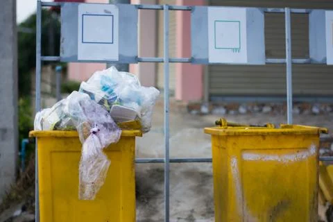 Yellow Garbage Trash Bin full of garbage  in small village at countryside Stockfoto's