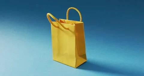 Yellow gift bag with string handles string on blue background Stock Footage 339589790