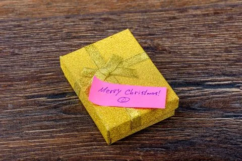 Yellow gift box with handwritten note Merry Christmas on wooden background. Stock Photos