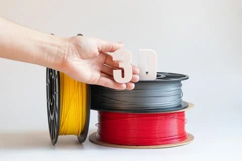 Yellow, gray, and red plastic filaments for 3D printing on spools and a fem.. Stock Photos