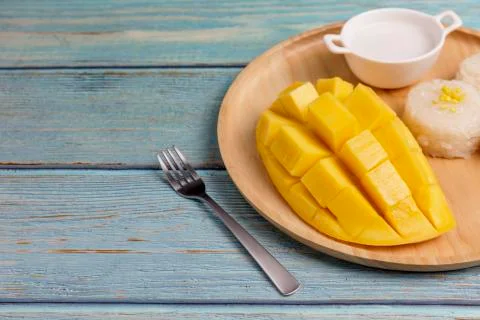 Yellow half  mango with small fork. Mango fruit cubes on the Blue wooden tabl Stock Photos