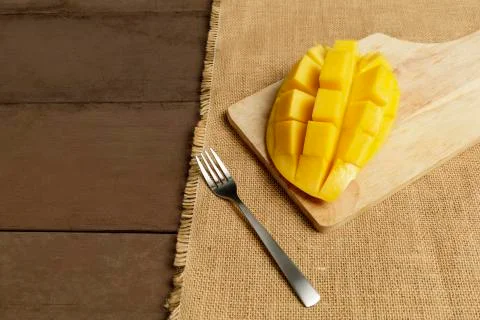 Yellow half  mango with small fork. Mango fruit cubes on the wooden table. Tr Stock Photos
