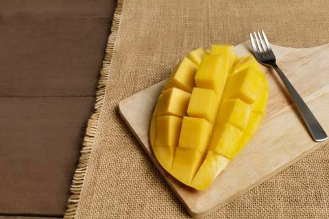 Yellow half  mango with small fork. Mango fruit cubes on the wooden table. Tr Stock Photos