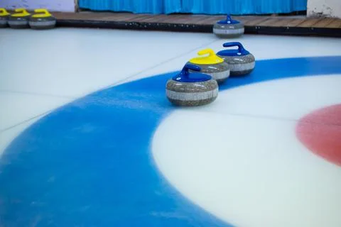 A yellow-handled stone stands between two blue-handled curling stones on the  Stock Photos