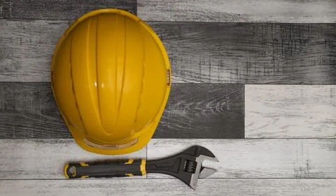 Yellow hard hat and adjustable wrench resting on wooden surface Stock Photos