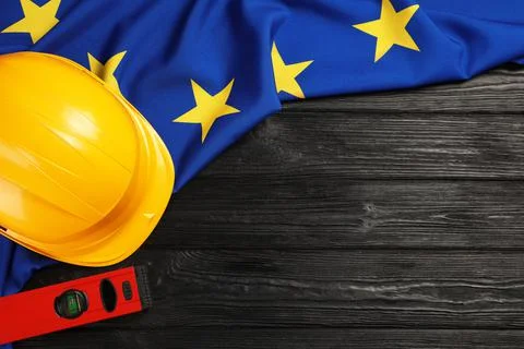Yellow hard hat, building level and flag of European Union on black wooden ta Fotos de archivo
