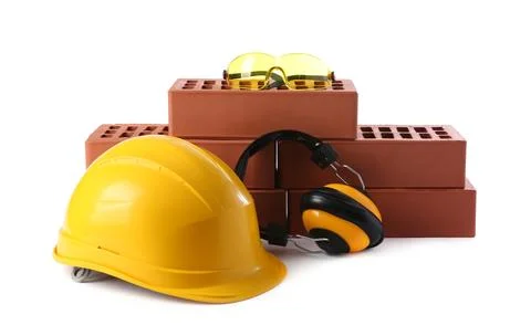 Yellow hard hat, red bricks, goggles and earmuffs isolated on white. Buildi.. Stock Photos