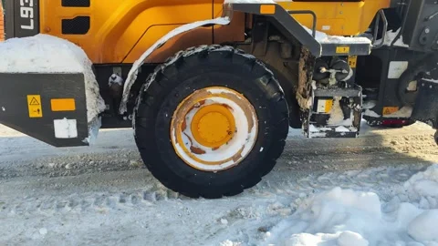 Yellow heavy equipment loader on snow-covered road with tire tracks under bright Stock Footage 342920796