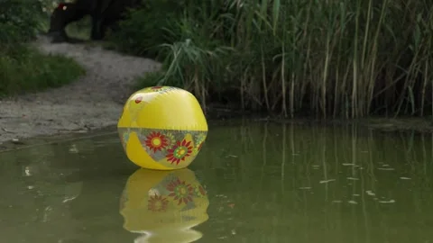 Yellow inflatable ball with floral pattern floats on calm water surface 動画素材 340844591