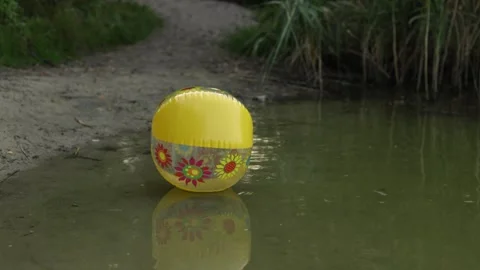 Yellow inflatable ball with floral pattern floats on murky water surface 動画素材 340844601