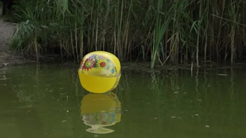 Yellow inflatable ball with floral pattern floats on calm water surface 動画素材 340844631