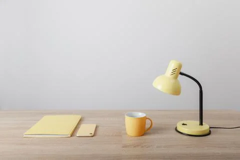 Yellow items notebook cup and lamp on wooden table Stock Photos