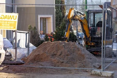 A yellow JCB excavator sits behind a wire fence next to a large pile of Stock Photos