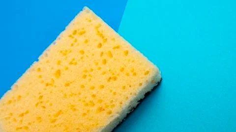 Yellow kitchen sponge on blue background. House cleaning. Household. Stock Photos
