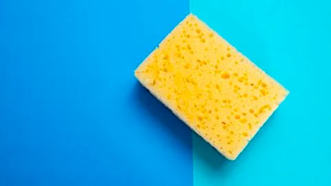 Yellow kitchen sponge on blue background. House cleaning. Household. Stock Photos
