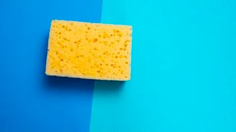 Yellow kitchen sponge on blue background. House cleaning. Household Stock Photos