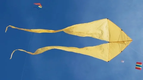 Yellow kite with two tails hovering in blue sky and sunny day Stock Footage 76265383