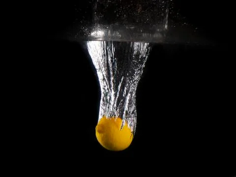 Yellow lemon falling into splashing water on black background Stock Photos