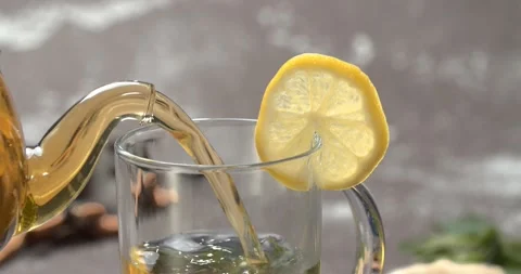 Yellow lemon tea from teapot into mint cup, slow motion, close up Stock Footage 142998620