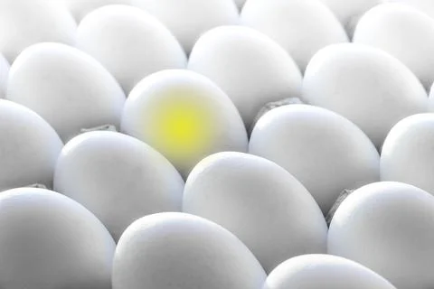 Yellow light in one egg among many white eggs.Creative concept photography. Stock Photos