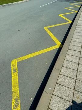 Yellow line marking forms a zigzag pattern on asphalt next to a sidewalk. The Stock Photos