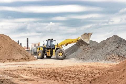A yellow loader is actively working at a construction site, moving piles of g Photos