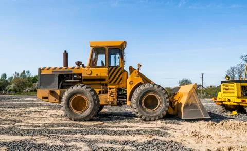 Yellow loader with empty bucket stands on a stone gravel during road Stock Photos