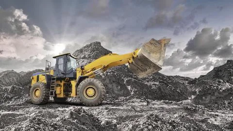 A yellow loader is working on a rocky construction site, moving large amounts 스톡 사진