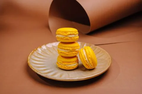 Yellow macarons stacked on a plate in a simple setup on a brown backdrop 写真素材
