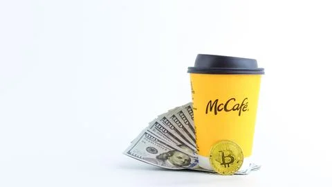 Yellow McCafe Coffee cup, surrounded by cash and cryptocurrency, symbolizing Stock Photos