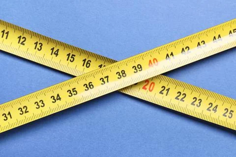 Yellow measuring tape intersecting on blue background, precision measurement  Stock Photos