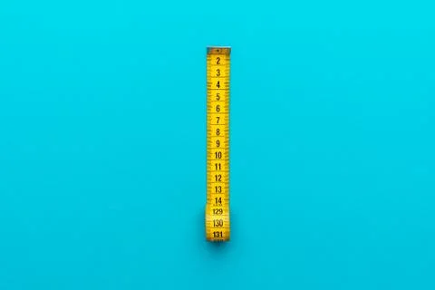 Yellow measuring tape on turquoise blue background with central composition Stock Photos