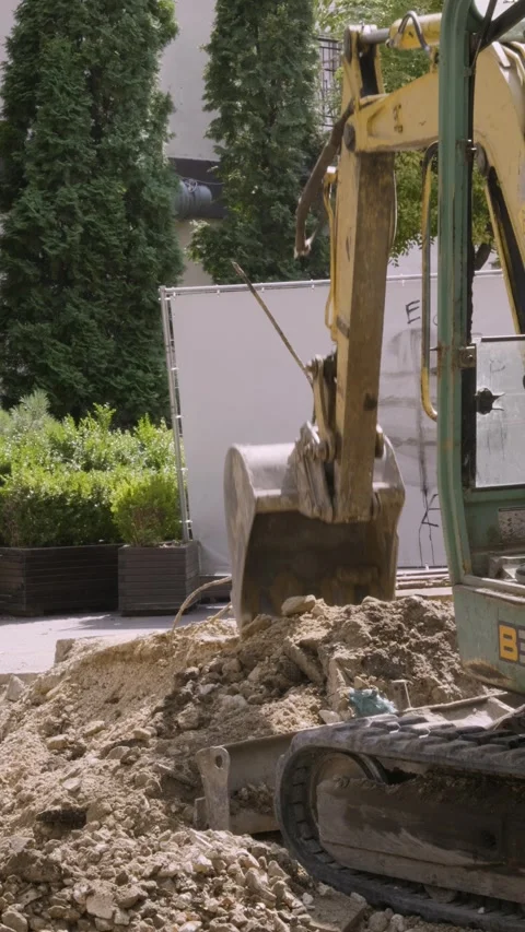 Yellow mini excavator digging dirt at urban construction site vertical b-roll Vidéo 345412271