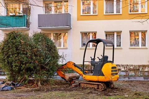 Yellow mini excavator in front of a multi-storey building next to a green bus Stock Photos
