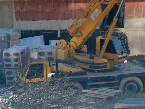 A yellow mobile crane stands at an active building site with stacked Stock Photos