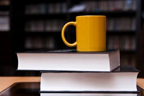 Yellow mug of coffee on the stack of books Stock Photos