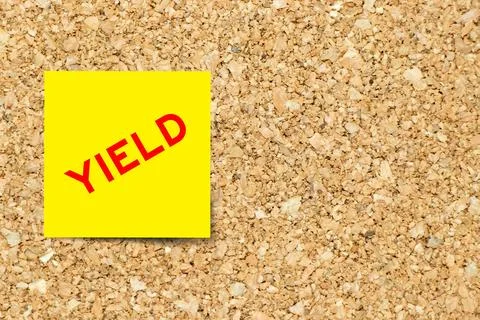 Yellow note paper with word yield on cork board background with copy space Stock Photos