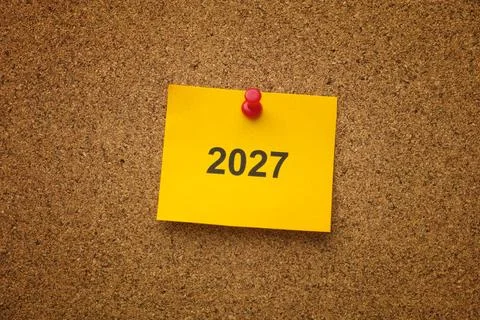 A yellow note with the year 2027 on it pinned to a cork board. Close up. Foto stock