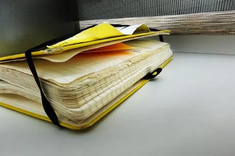 A yellow notebook sits on a table, with its pages slightly worn. Papers are p Stock Photos